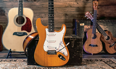 acoustic guitar, electric guitar, and two ukuleles in front of wood panels