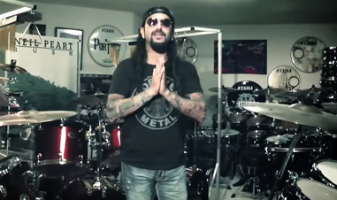 man with hands together surrounded by drum kits