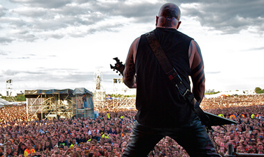 back view of man playing electric guitar on stage in front of large crowd